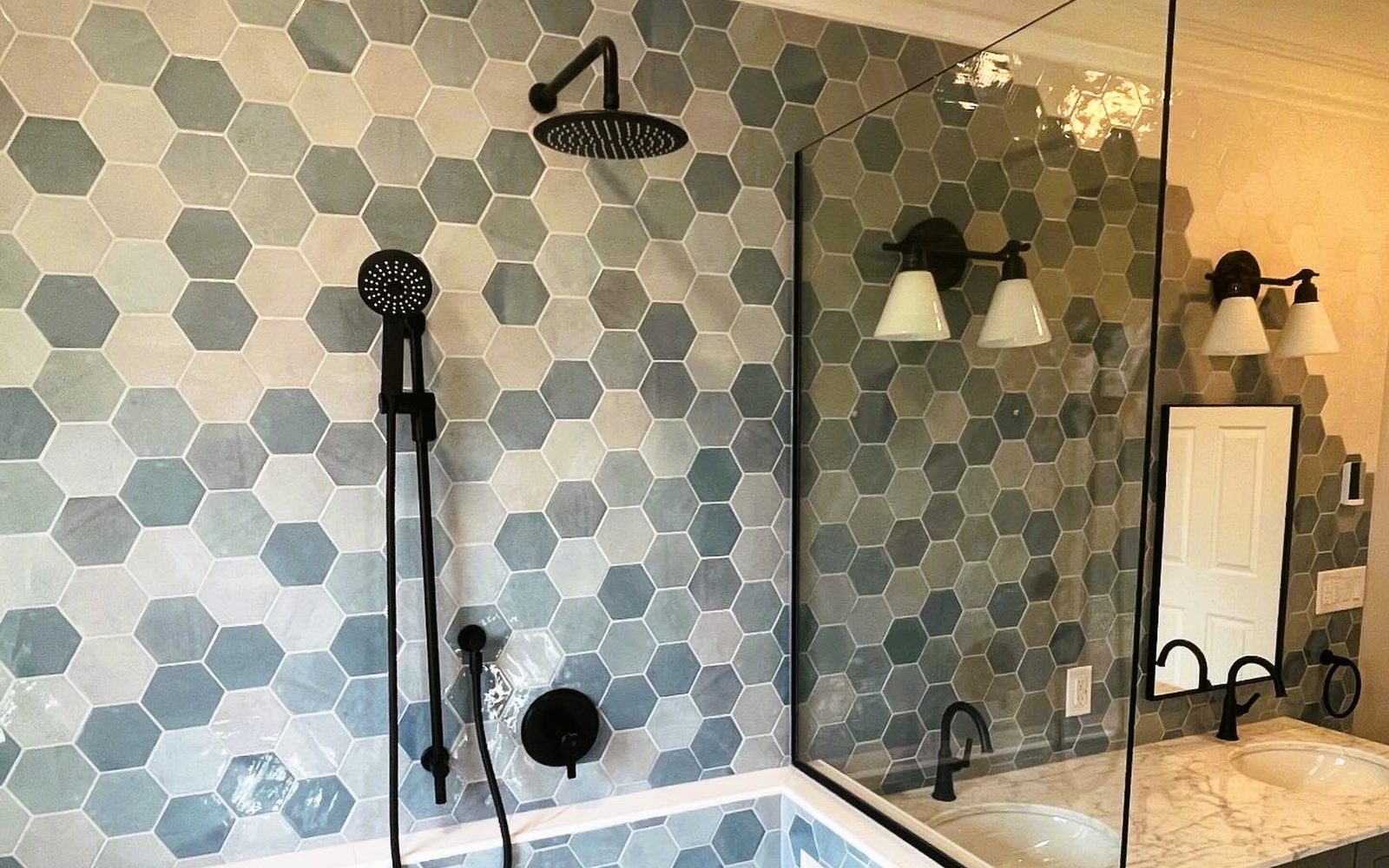 Finished wet-room ensuite built by Lions Group: blue hexagon tile shower with matte black rain shower and handheld, double vanity behind glass