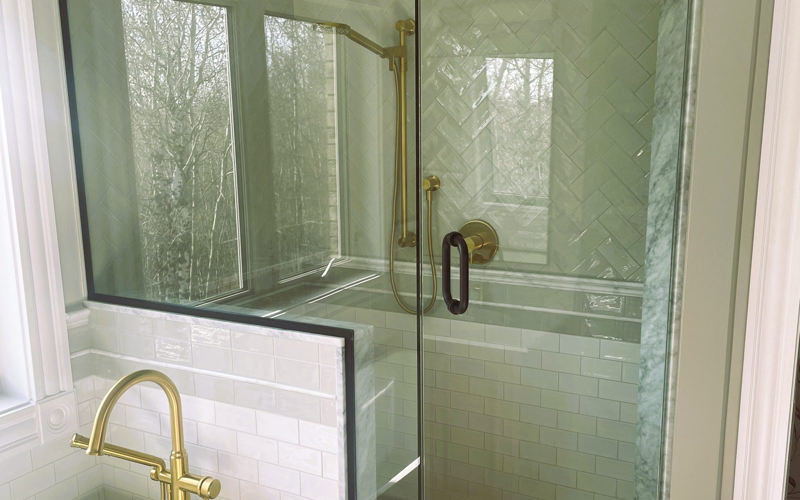 Finished ensuite built by Lions Group: glass shower with marble herringbone tile, brass shower fixtures and a brass freestanding tub filler