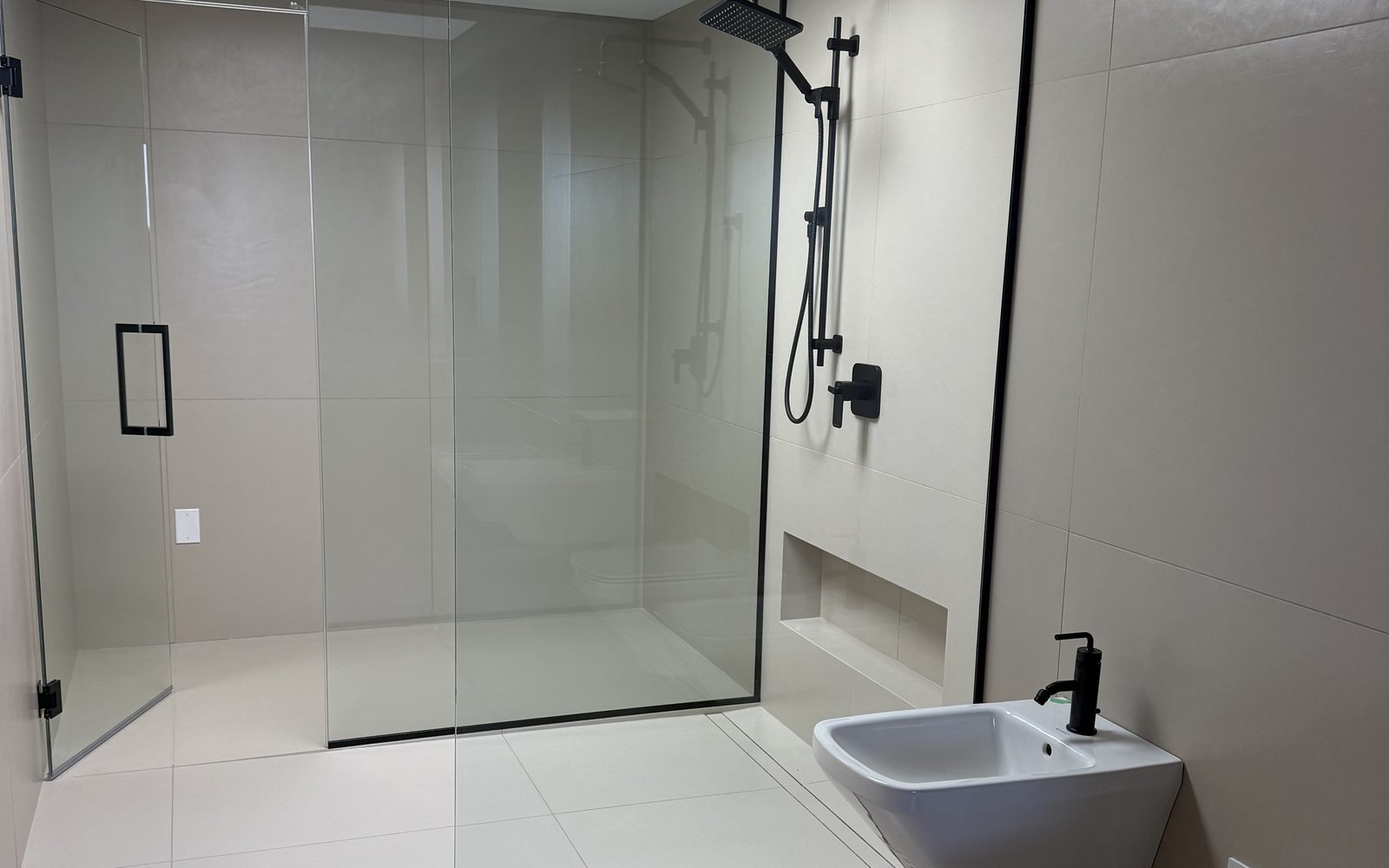 Finished wet room built by Lions Group: all-white large-format tile, glass shower enclosure, matte black fixtures and wall-hung fixtures