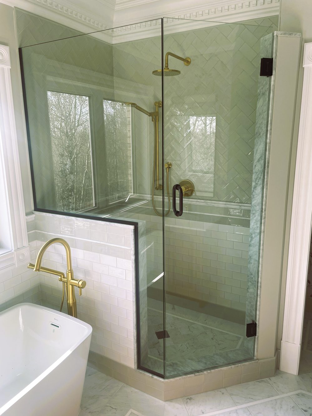 Finished ensuite by Lions Group: glass shower and freestanding tub with marble herringbone tile and brass fixtures