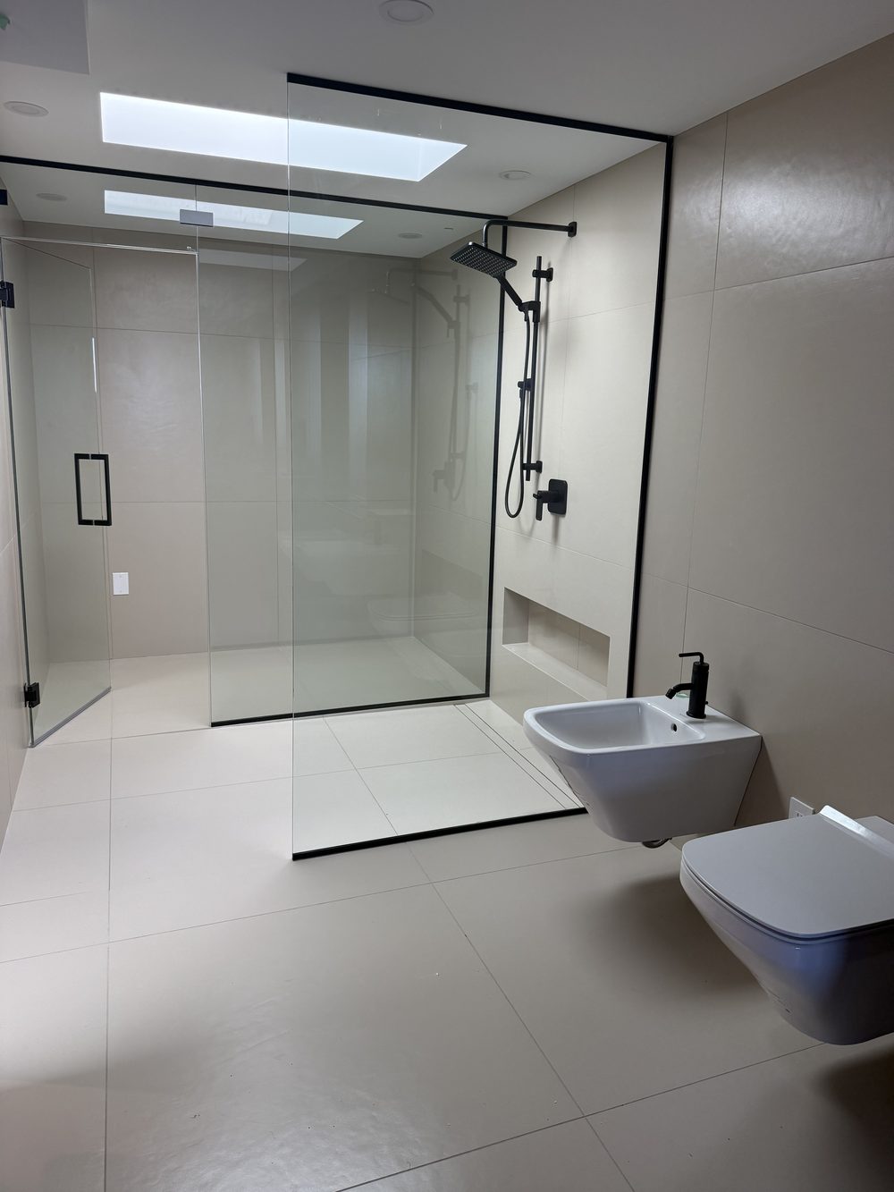 Finished wet room by Lions Group: all-white large-format tile with wall-hung fixtures